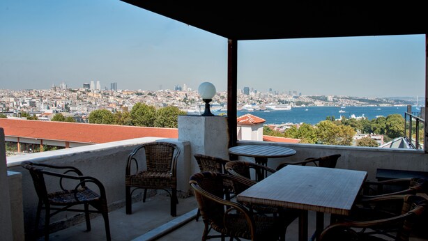 A balcony with wicker furniture and a table, overlooking a cityscape and the sea. - Le Safran Palace (Istanbul)