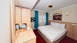 A hotel room with a wooden desk, a bed with white linens, a large mirror, a ceiling light, and a window with blue curtains. - Le Safran Palace (Istanbul)