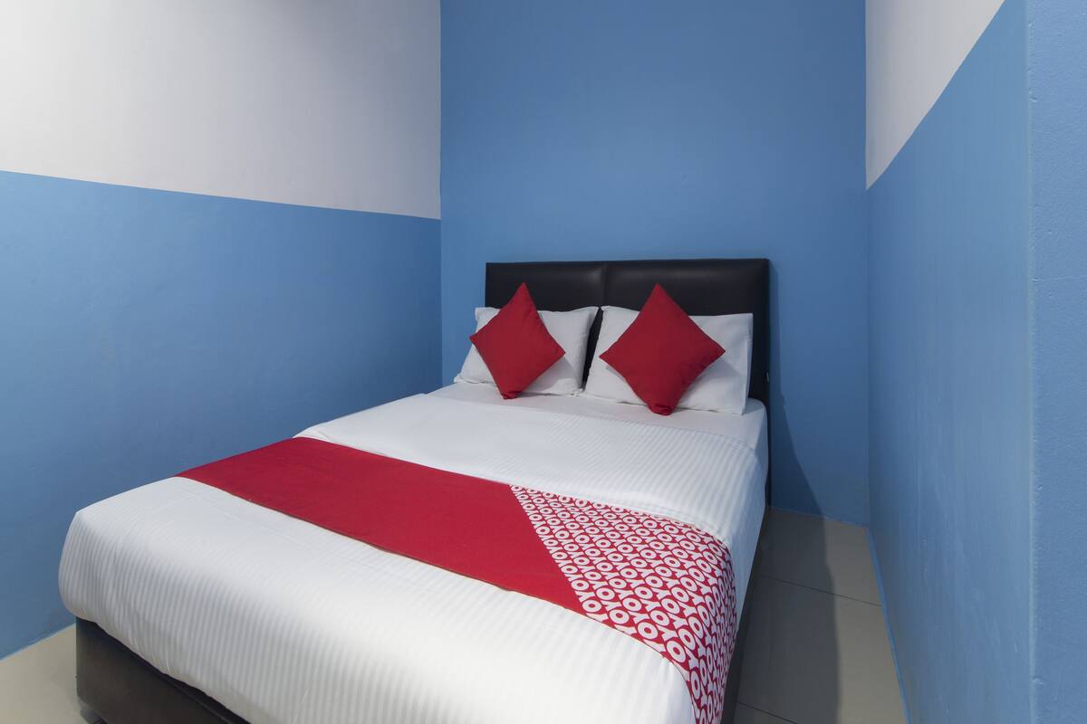 Una habitación de hotel con cama, ropa de cama blanca y roja, y una pared de acento azul.