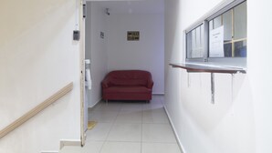 Un couloir étroit avec un canapé rouge, un escalier et une fenêtre sur laquelle est apposée une enseigne.