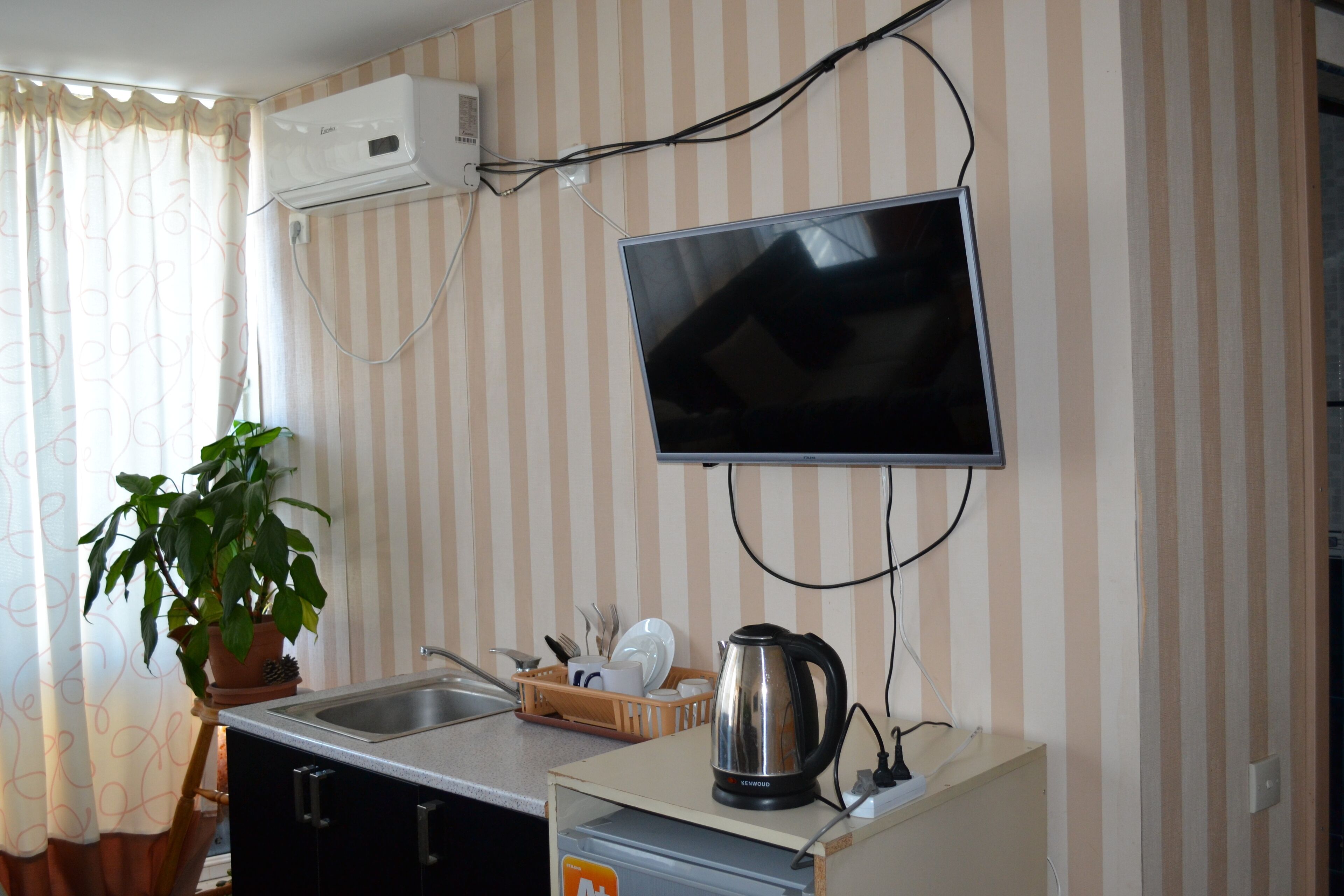 Una kitchenette con estufa integrada, un lavamanos y un televisor de pantalla plana montado en la pared.