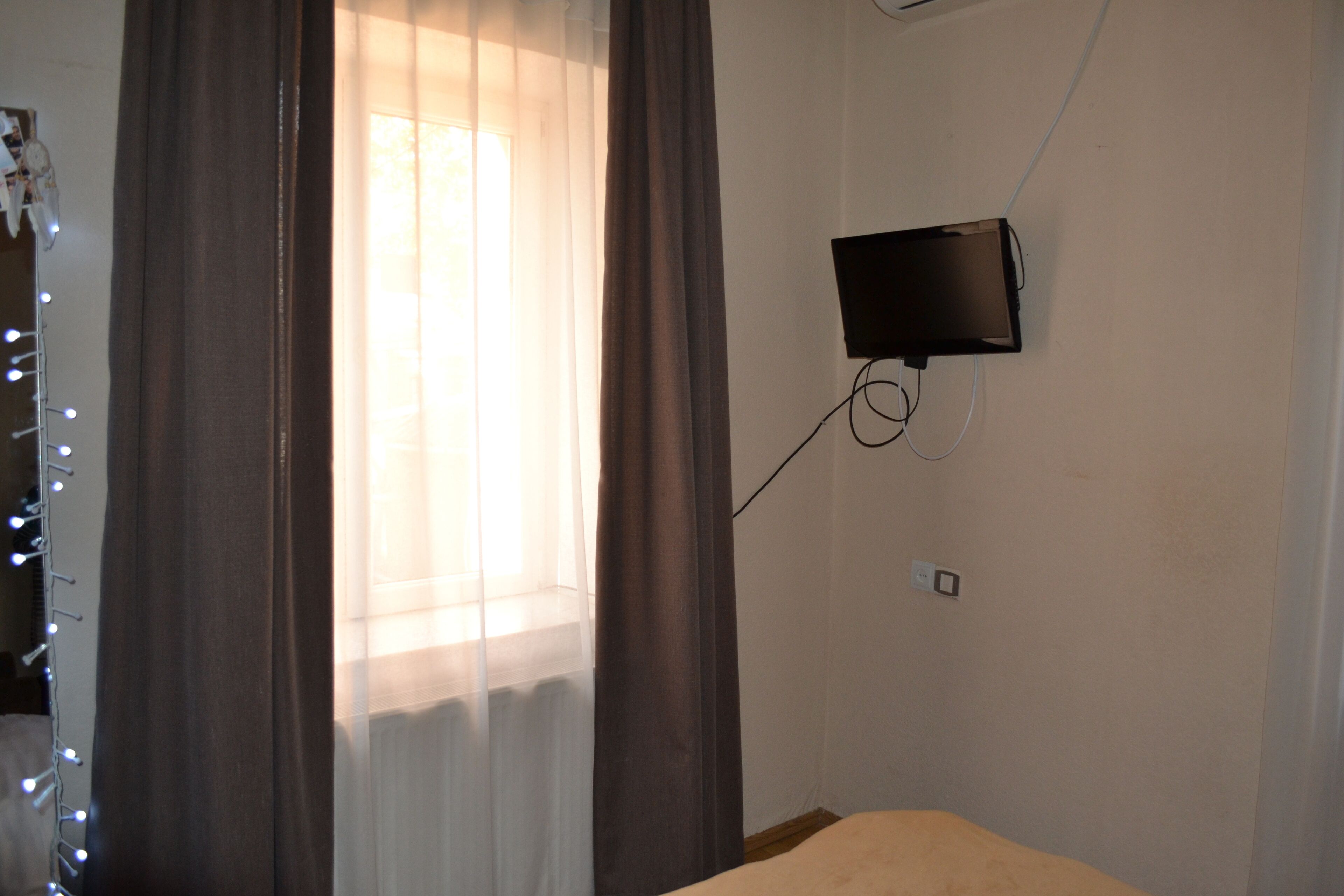 A room with a bed, a wall-mounted television, and a window with curtains.