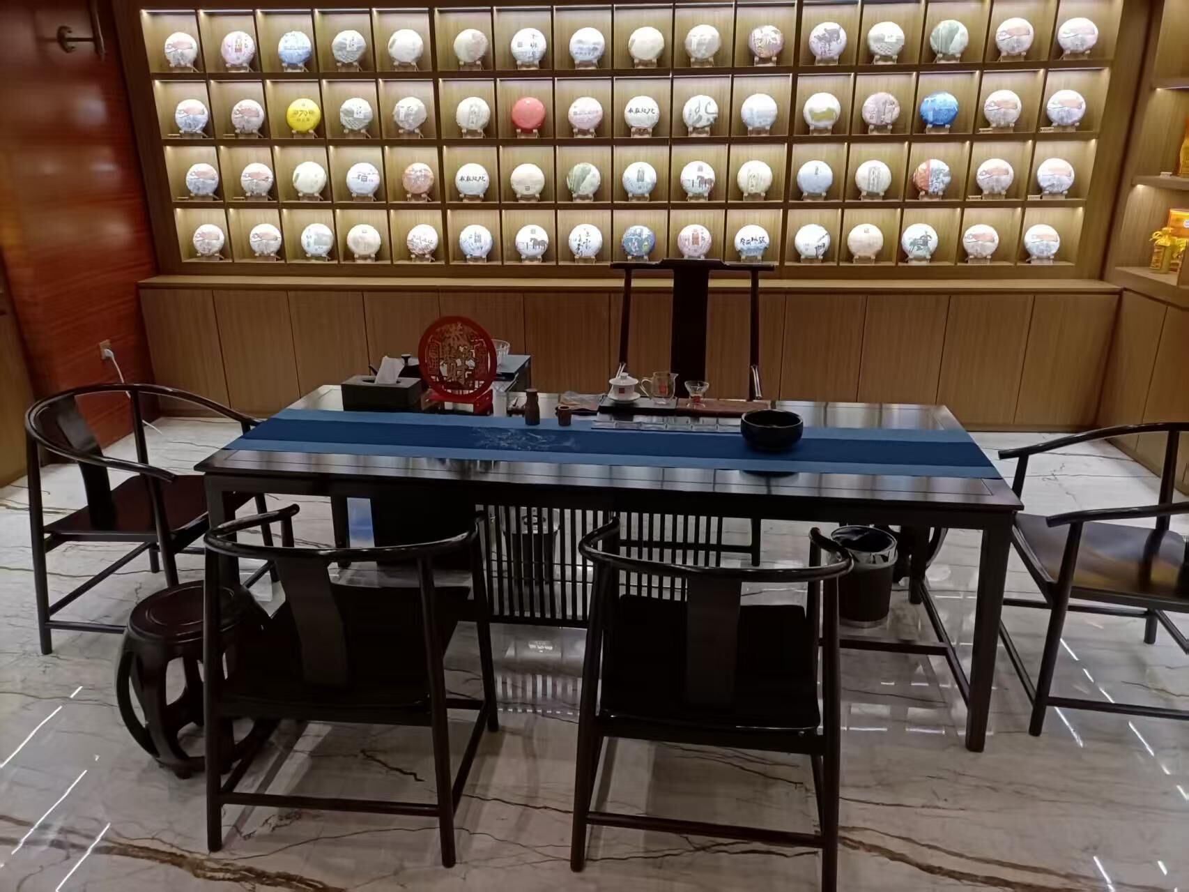 Un comedor con una mesa larga, cuatro sillas, una placa decorativa roja y una pared de objetos redondos iluminados.