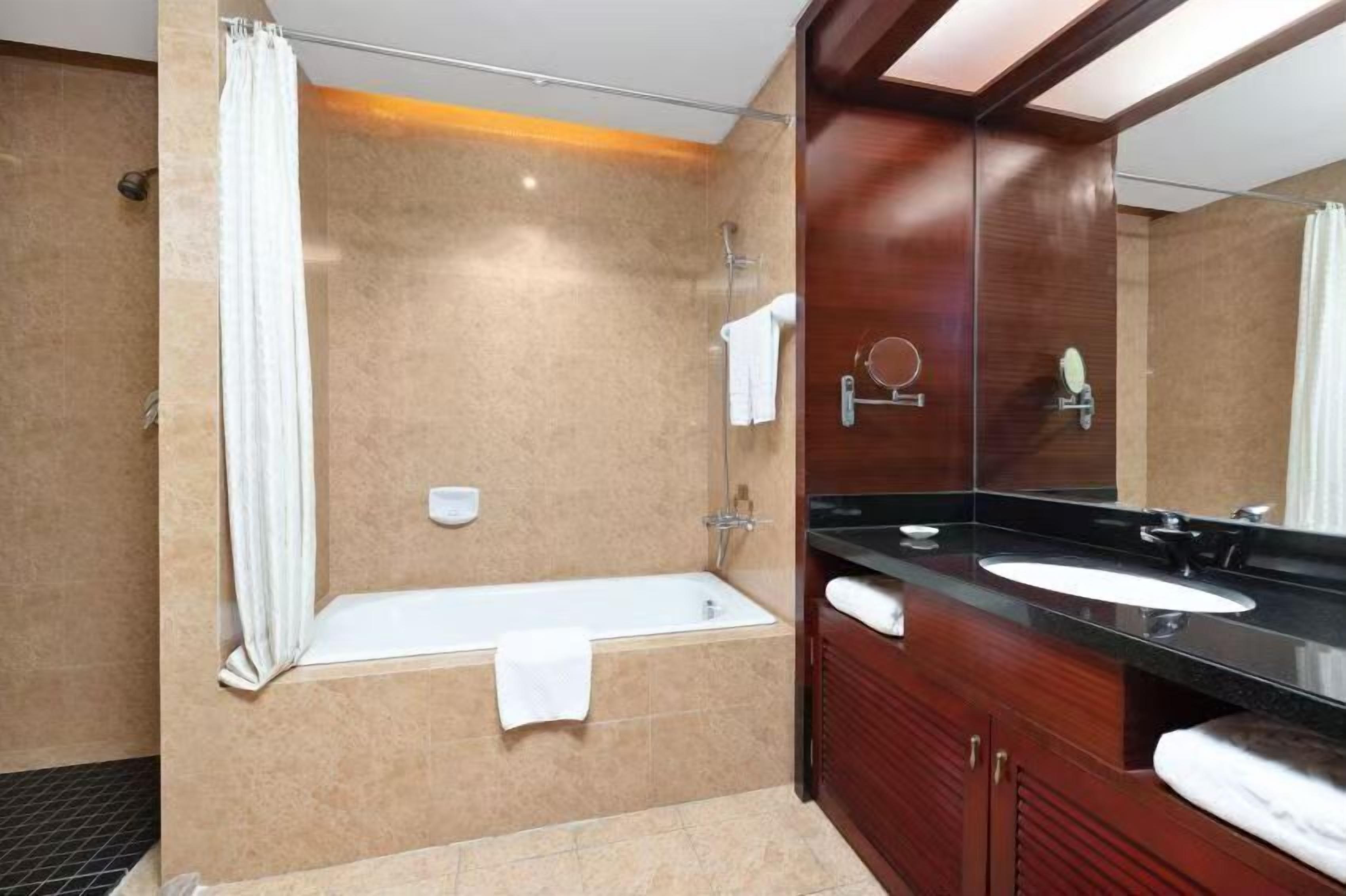 A modern bathroom with a bathtub, a large mirror, and a vanity with a sink.