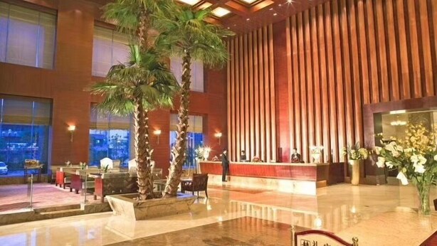 A hotel lobby with a reception desk, palm trees, and a modern interior design. - Shenzhen Kaijia Hotel (Shenzhen)