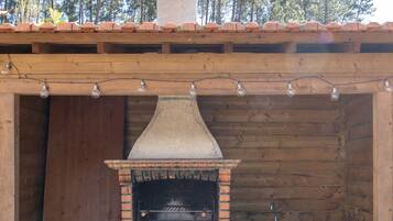 An outdoor brick oven with a chimney, a sink, and a shelf with firewood.