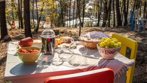 A table set outdoors with a bottle, glasses, strawberries, grapes, and bread.