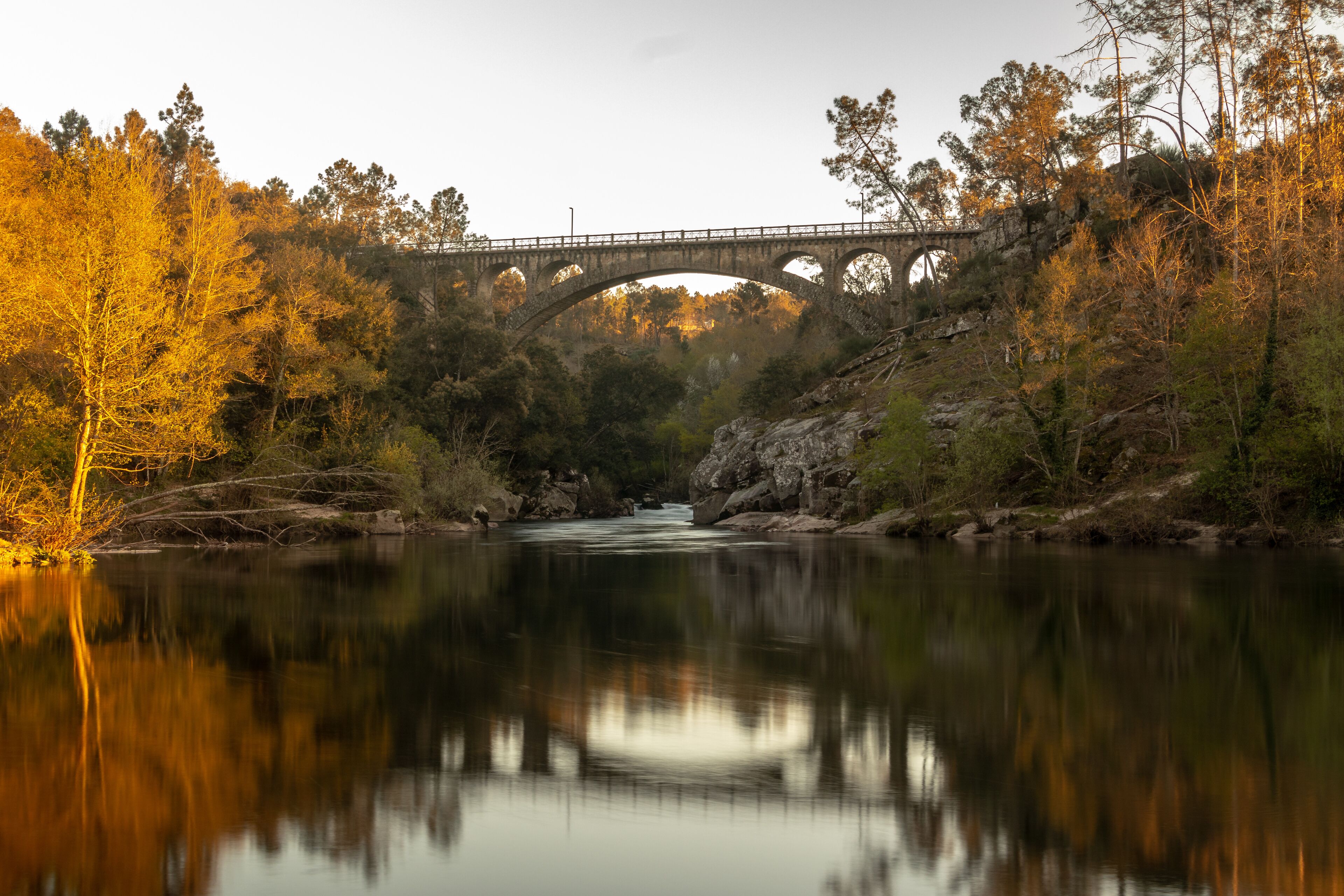 A stone bridge over a calm river with autumn foliage on either side.
