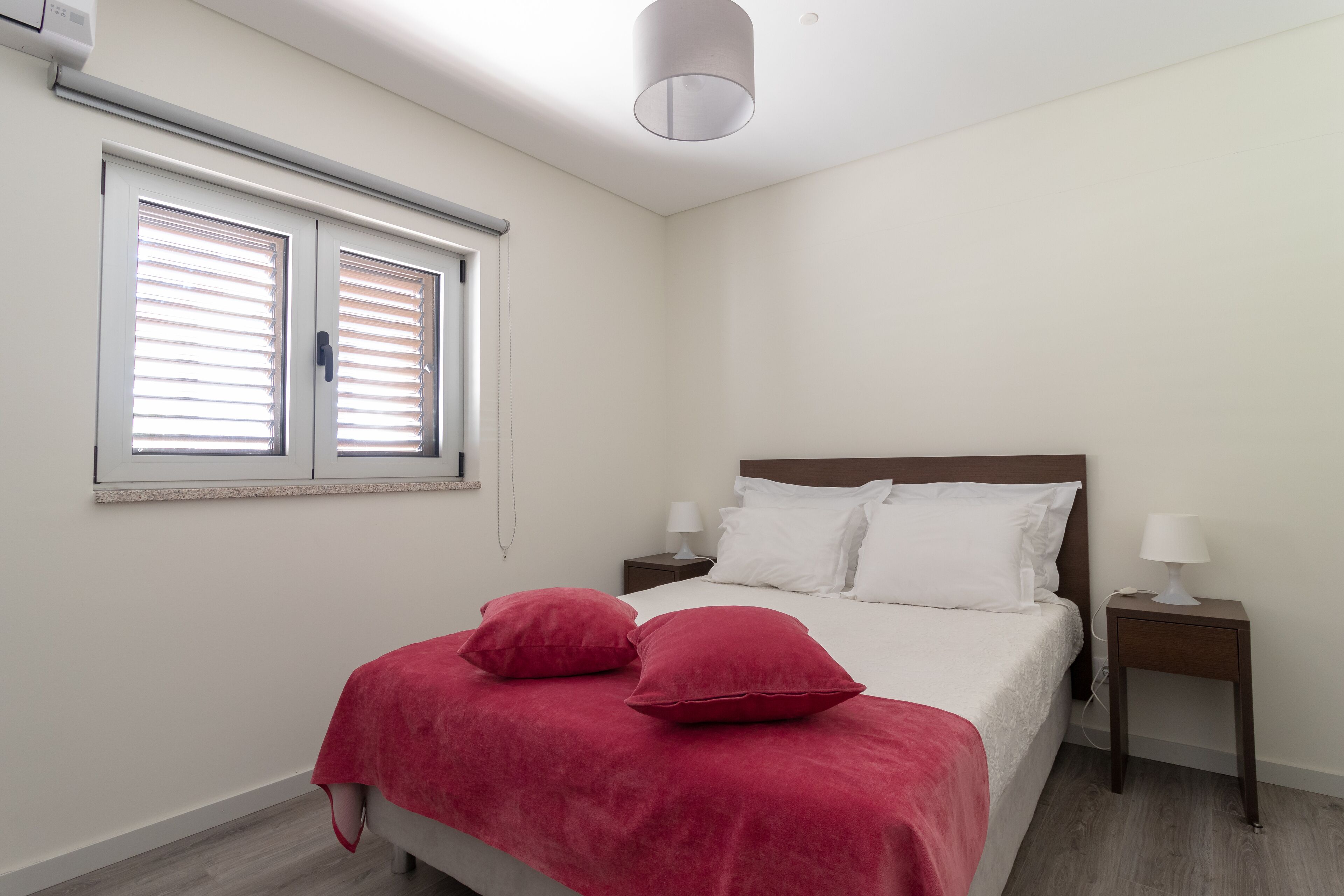 Una camera da letto con un letto, due comodini, una finestra con persiane e una lampada a soffitto.