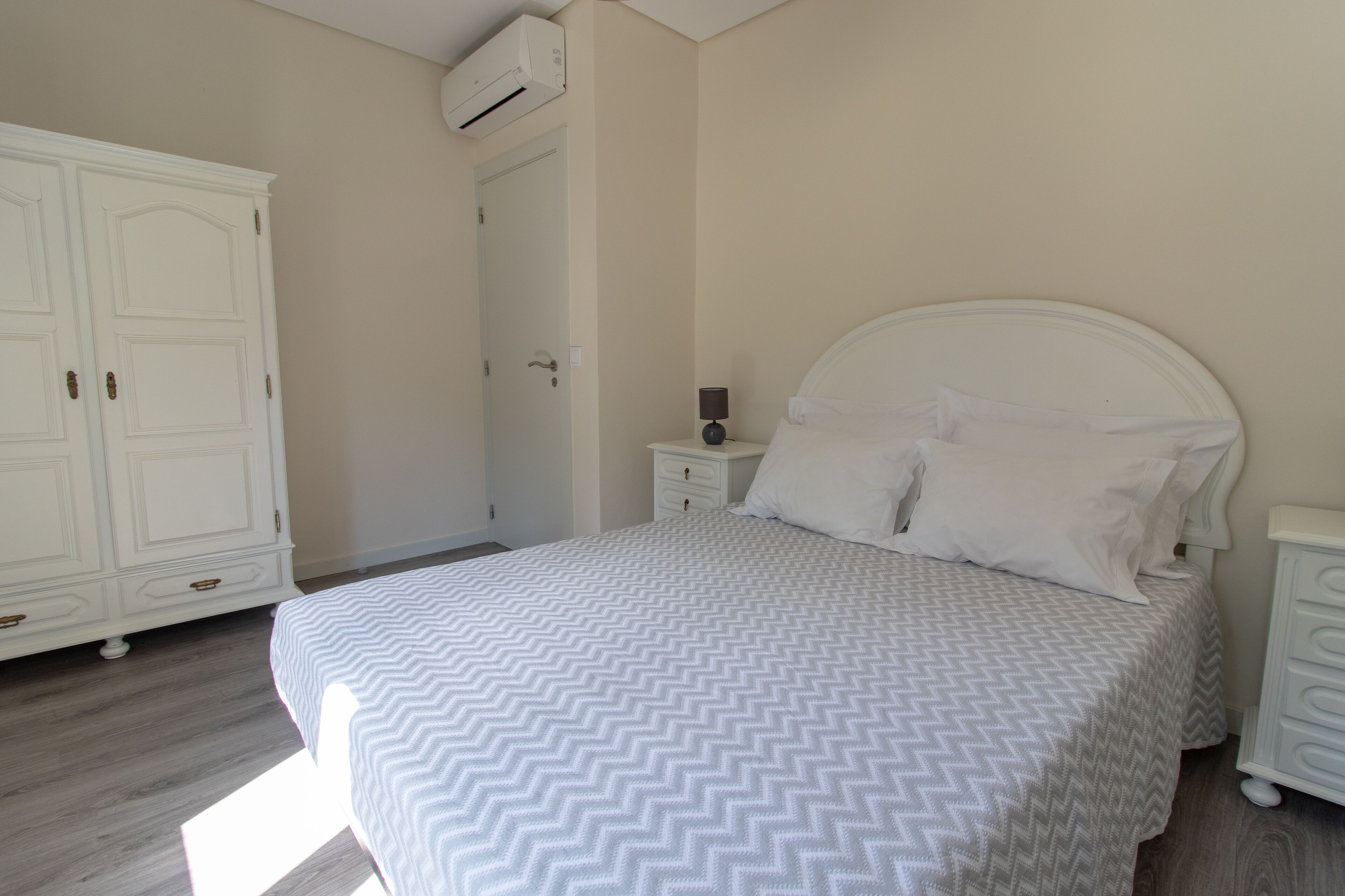 A bedroom with a bed, a nightstand, a dresser, and an air conditioning unit.