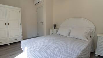 A bedroom with a bed, a nightstand, a dresser, and an air conditioning unit.