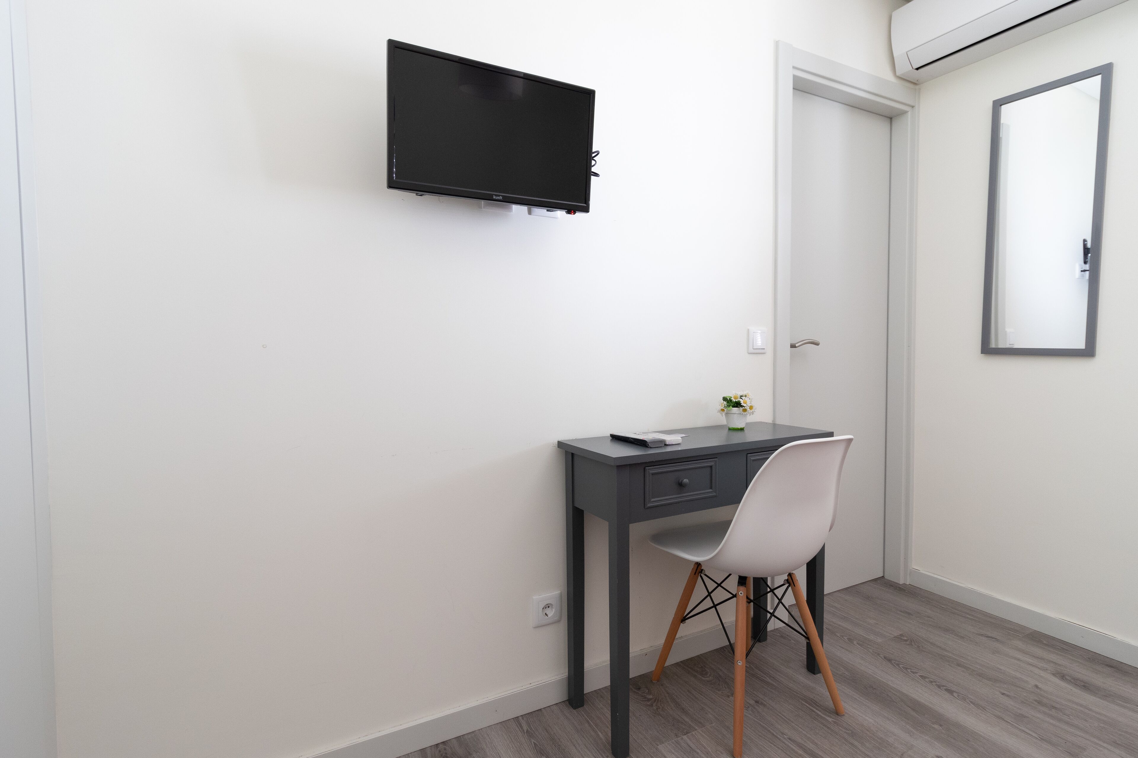 Ein kleiner, moderner Raum mit Schreibtisch, Stuhl und einem Wand-Fernseher.
