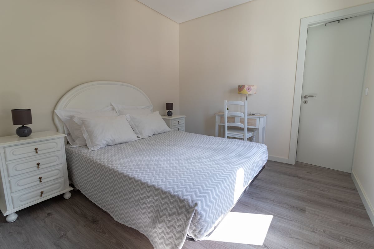 A bedroom with a bed, nightstands, a chair, and a door.