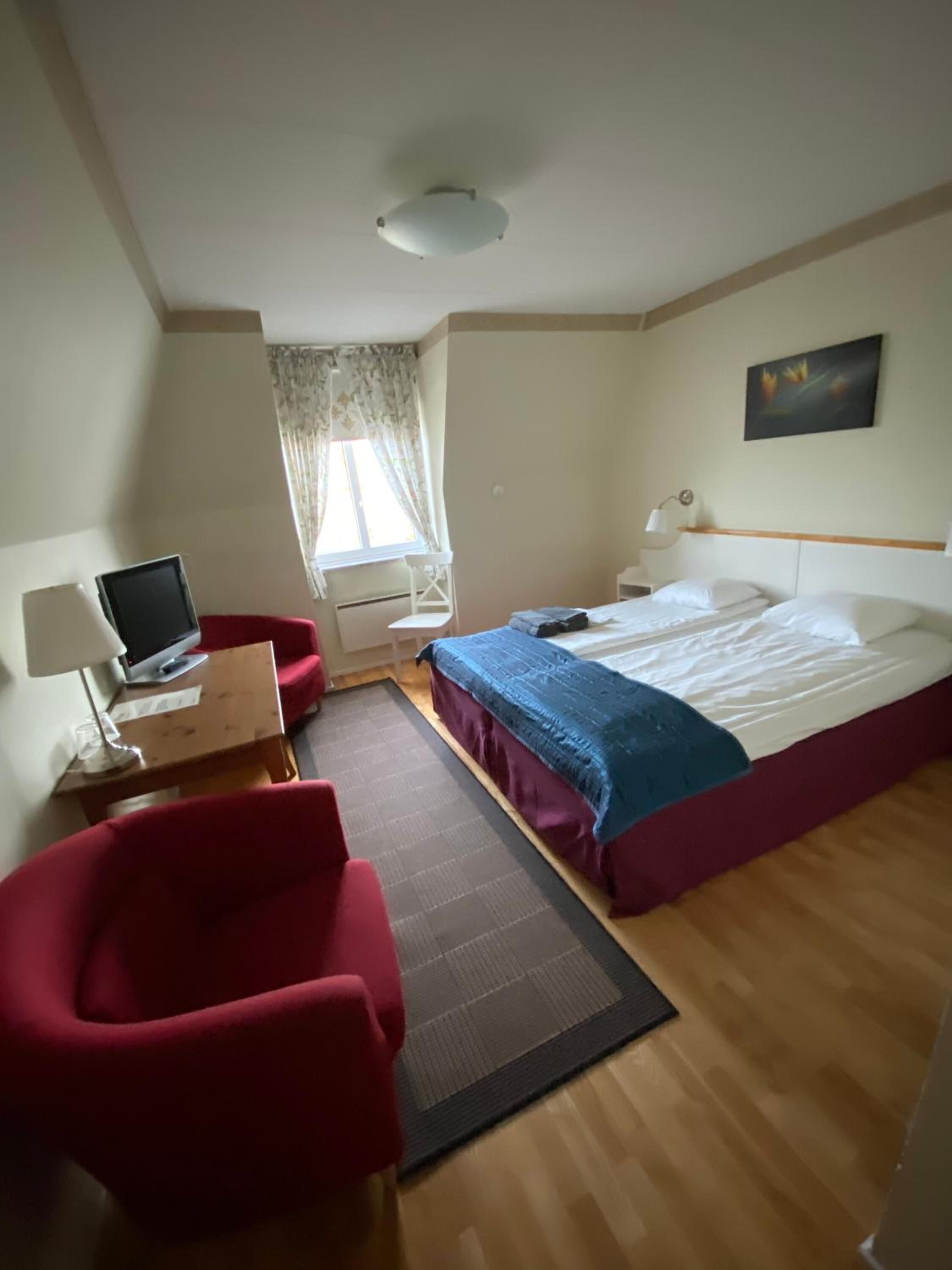 A hotel room with a bed, a desk with a computer, a chair, and a window with curtains.