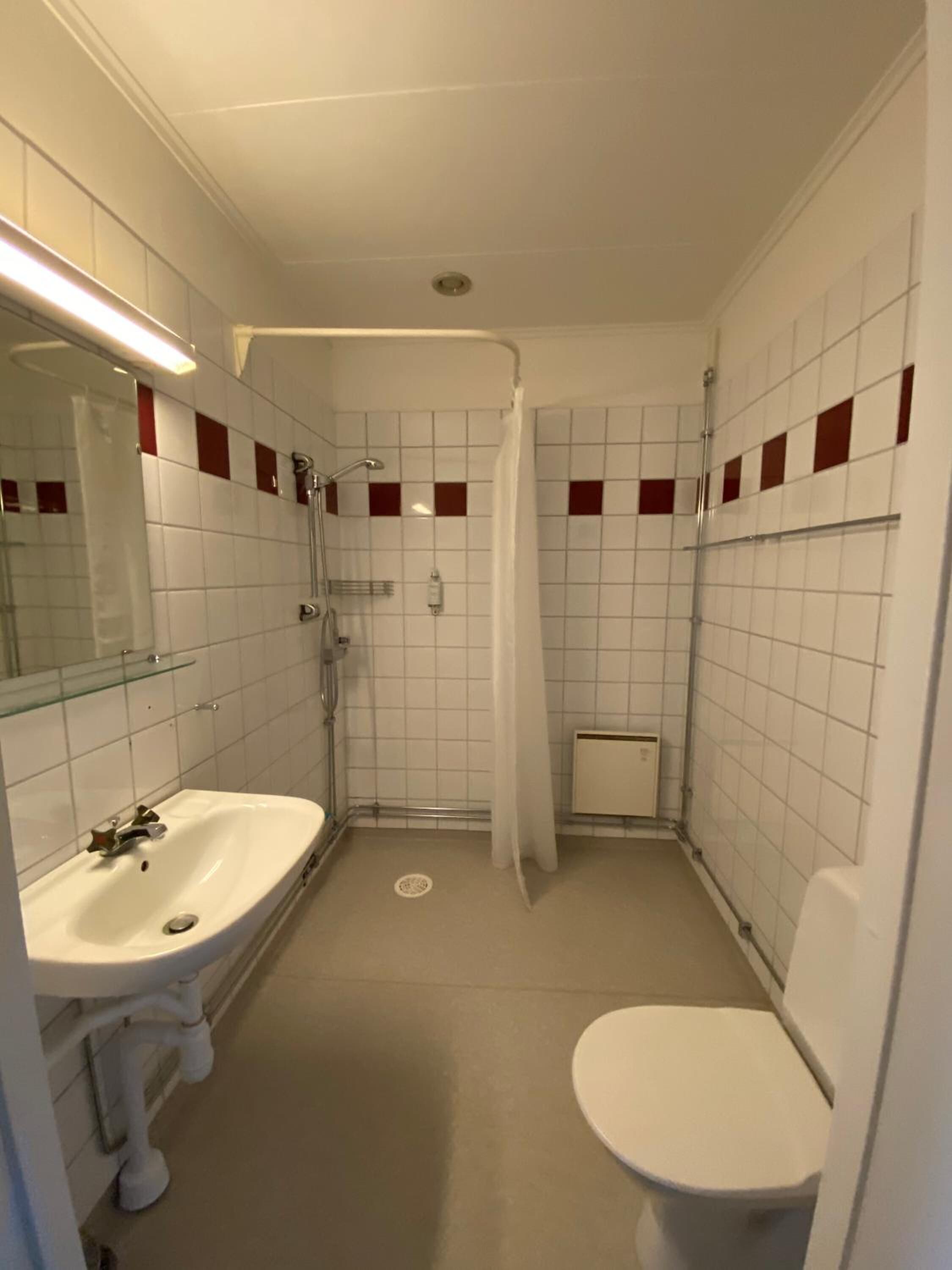 A small, compact bathroom with a white sink, toilet, and shower area.