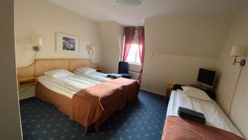 Ett hotellrum med två sängar, ett skrivbord med en dator, en TV och ett fönster med gardiner.
