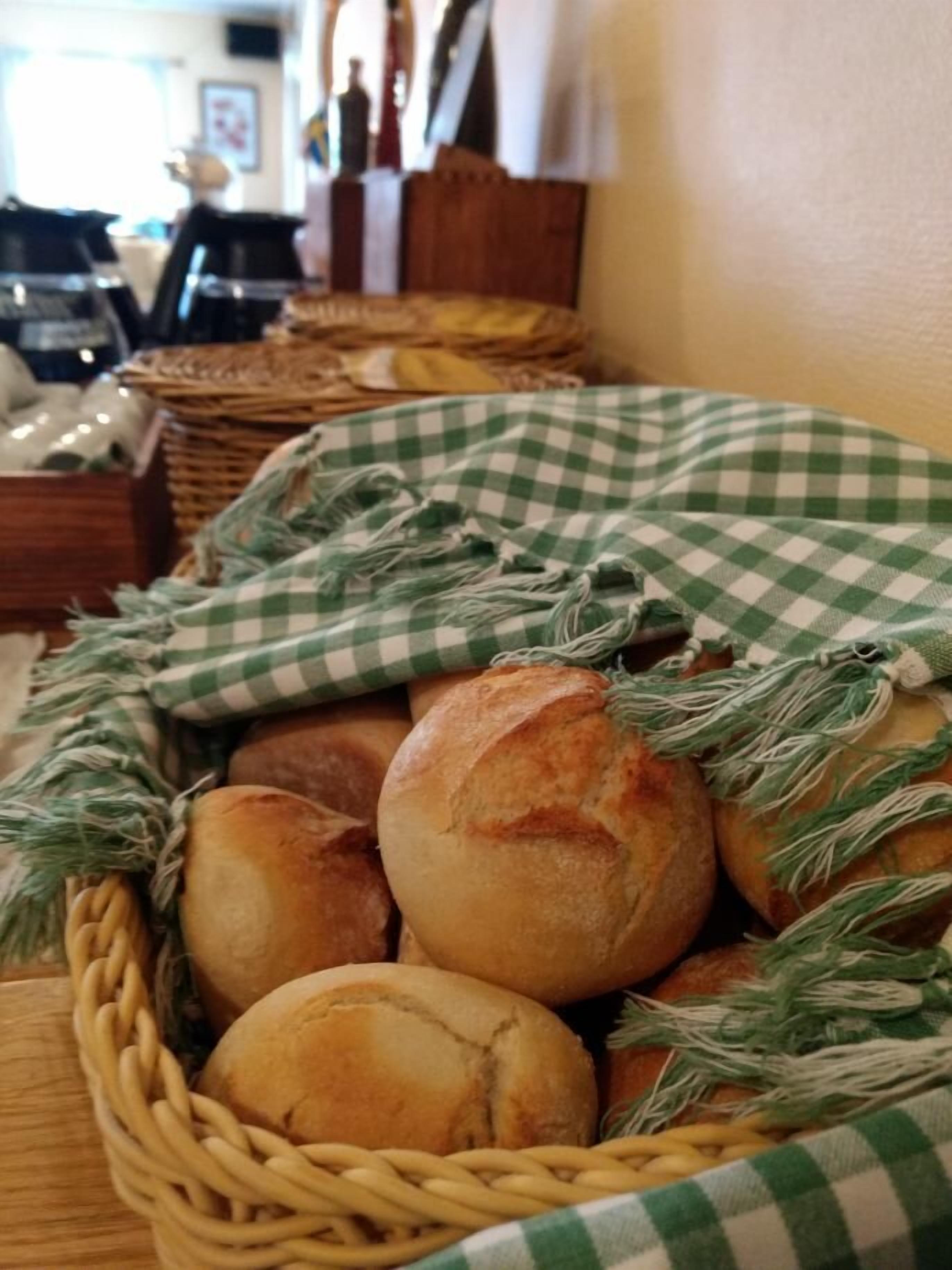 Una cesta con panecillos recién horneados, algunos envueltos en un paño de cuadros verdes y blancos, sobre una mesa de madera.