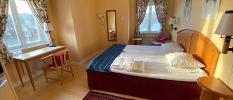 Habitación de hotel con cama, escritorio, silla y alfombra roja estampada.