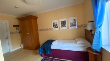 Un dormitorio con cama, armario de madera, alfombra estampada y pared con tres cuadros.