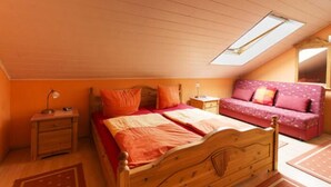 A bedroom with a sloped ceiling, a skylight, a wooden bed, a nightstand, a red and white sofa, and a patterned rug. - Gästehaus Walter (Offenbach an der Queich)
