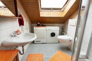 A compact bathroom with a skylight, a sink, a washing machine, and a toilet.