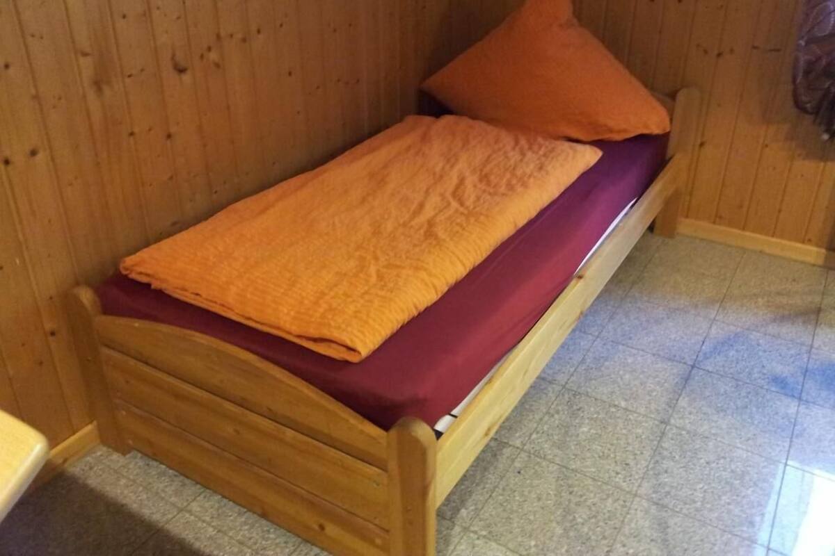 A single wooden bed with a red mattress and an orange blanket.