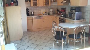 A compact kitchen with wooden cabinets, a microwave, a coffee maker, and a small dining area with metal chairs. - Gästehaus Walter (Offenbach an der Queich)
