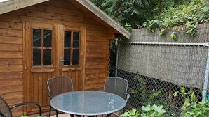 A wooden cabin with a fenced patio, a round table, and metal chairs. - Gästehaus Walter (Offenbach an der Queich)