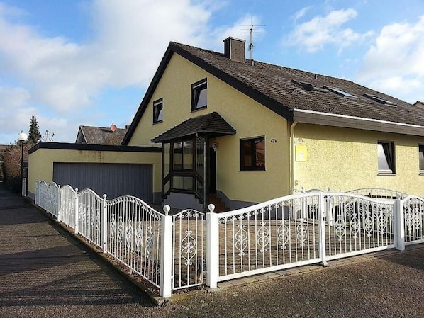 A two-story house with a garage, a covered porch, and a white fence.