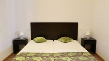 A double bed with a dark headboard, two green pillows, and a floral-patterned bedspread. There are two bedside tables with lamps.