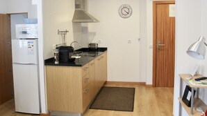 Eine kleine Küche mit Mikrowelle, Kaffeemaschine und Toaster auf der Arbeitsfläche. An der Wand hängt eine Uhr und es gibt eine Tür mit einem Hinweisschild.
