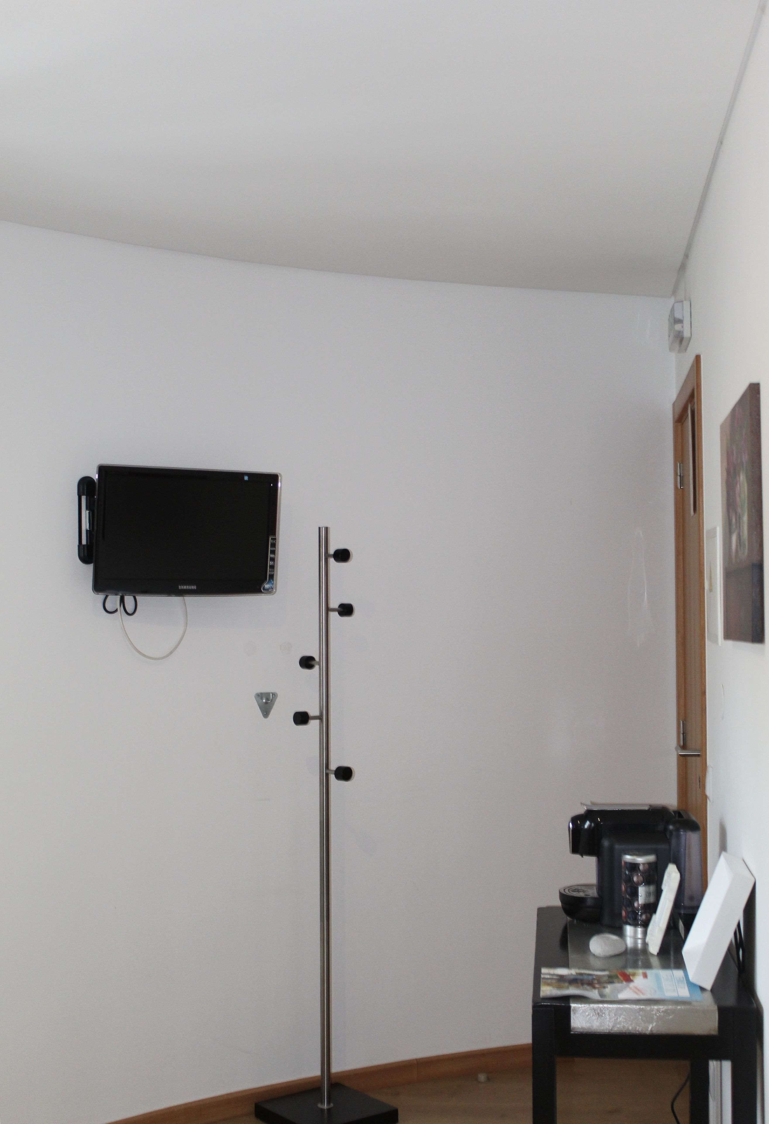 Una stanza con televisione a parete, una scrivania con macchina del caffè e un ripiano fissato al muro.