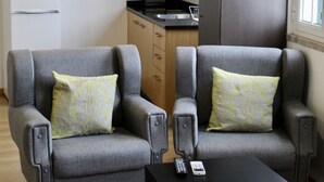 Ein modernes Wohnzimmer mit zwei grauen Sesseln, einem schwarzen Couchtisch und einer Küche im Hintergrund.