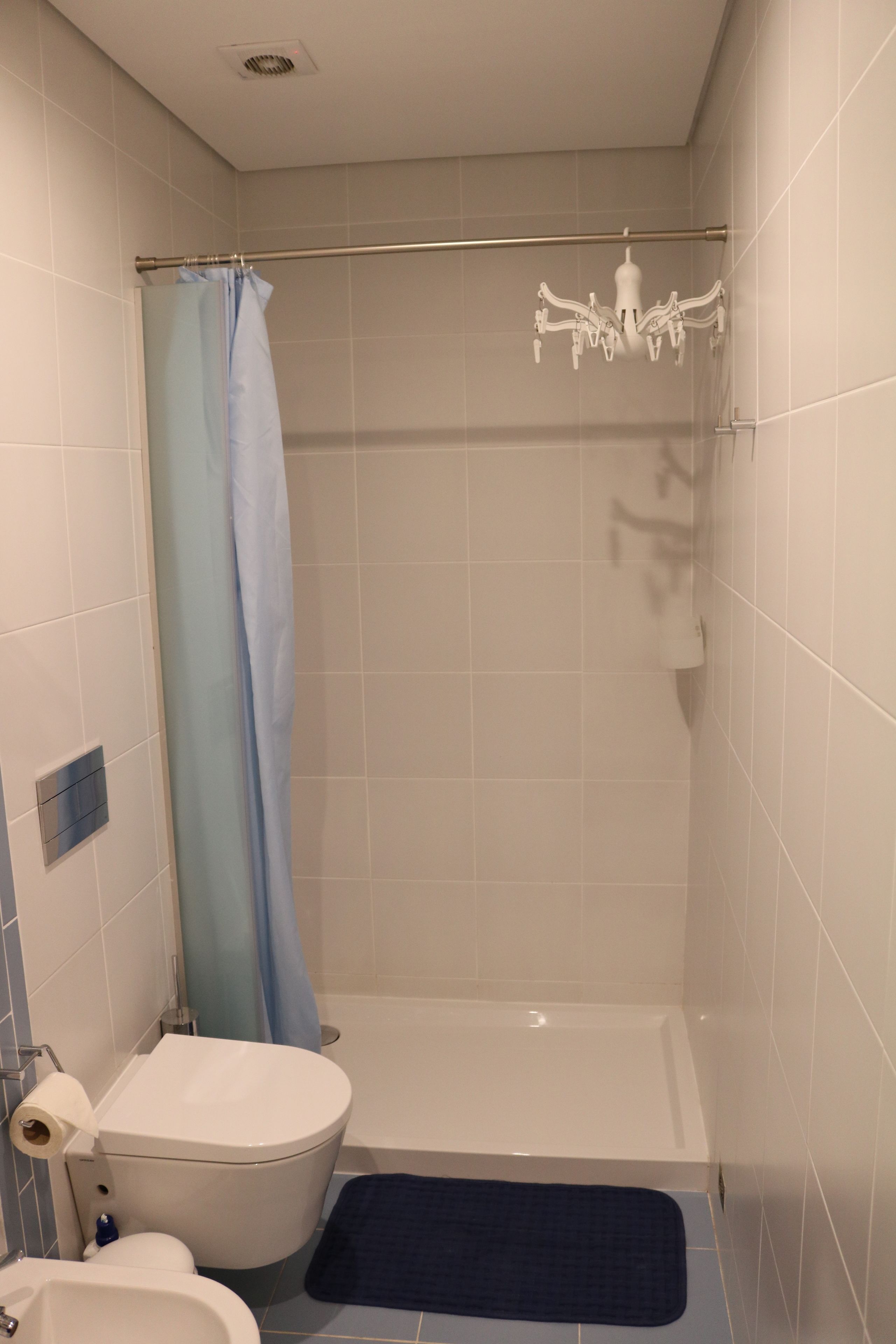 A bathroom with a toilet, bathtub, shower curtain, and a blue bath mat.