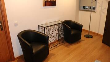 A room with two black leather chairs, a glass-top table with a decorative metal frame, a wooden floor, and a wall-mounted air conditioning unit.