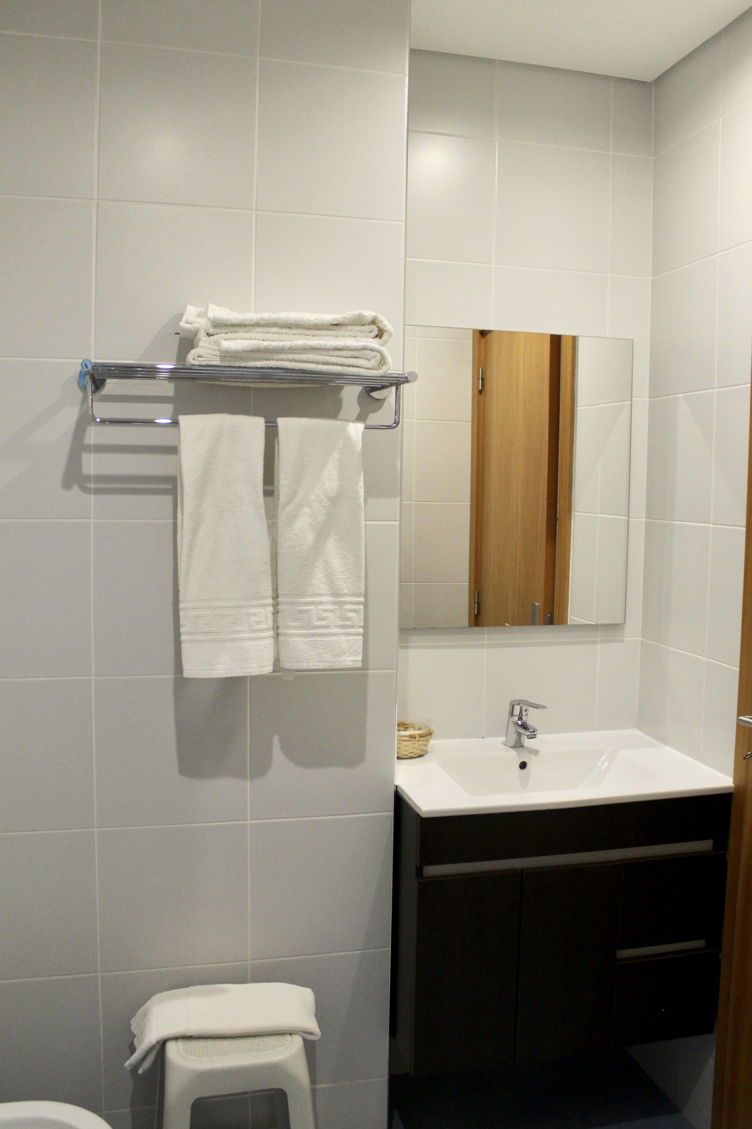 Un bany amb parets revestides de rajoles blanques, un lavabo blanc, un mirall i un portaTo soles amb tovalloles dobles.