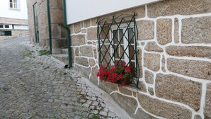 Eine Kopfsteinpflasterstraße mit einem Steinhaus, das ein Fenster mit einem Metallgitter und roten Blumen zeigt.