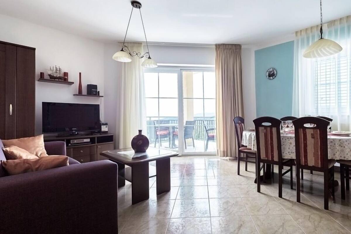 A living room with a sofa, TV, and dining area with chairs and a table.
