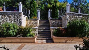 A stone staircase leading to a gated entrance, surrounded by lush greenery and a tiled pathway. - Apartments Villa Venera (Labin)