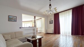 A living room with a sofa, a small table, a chandelier, and a large window with curtains. - Apartments Villa Venera (Labin)