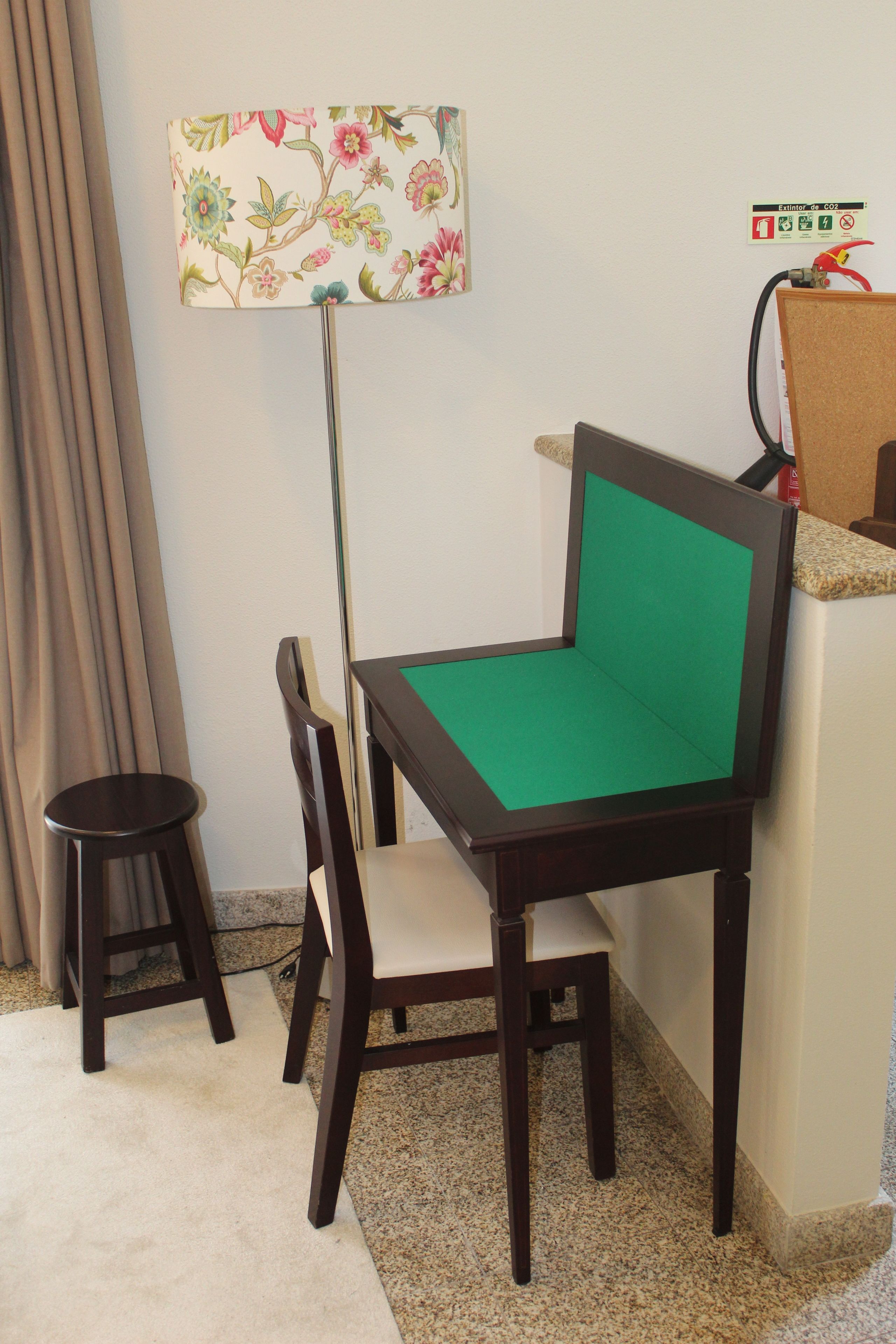 Une pièce comprenant un fauteuil rembourré de couleur verte, un petit tabouret, une lampe à motifs floraux et un extincteur à dioxyde de carbone fixé au mur.