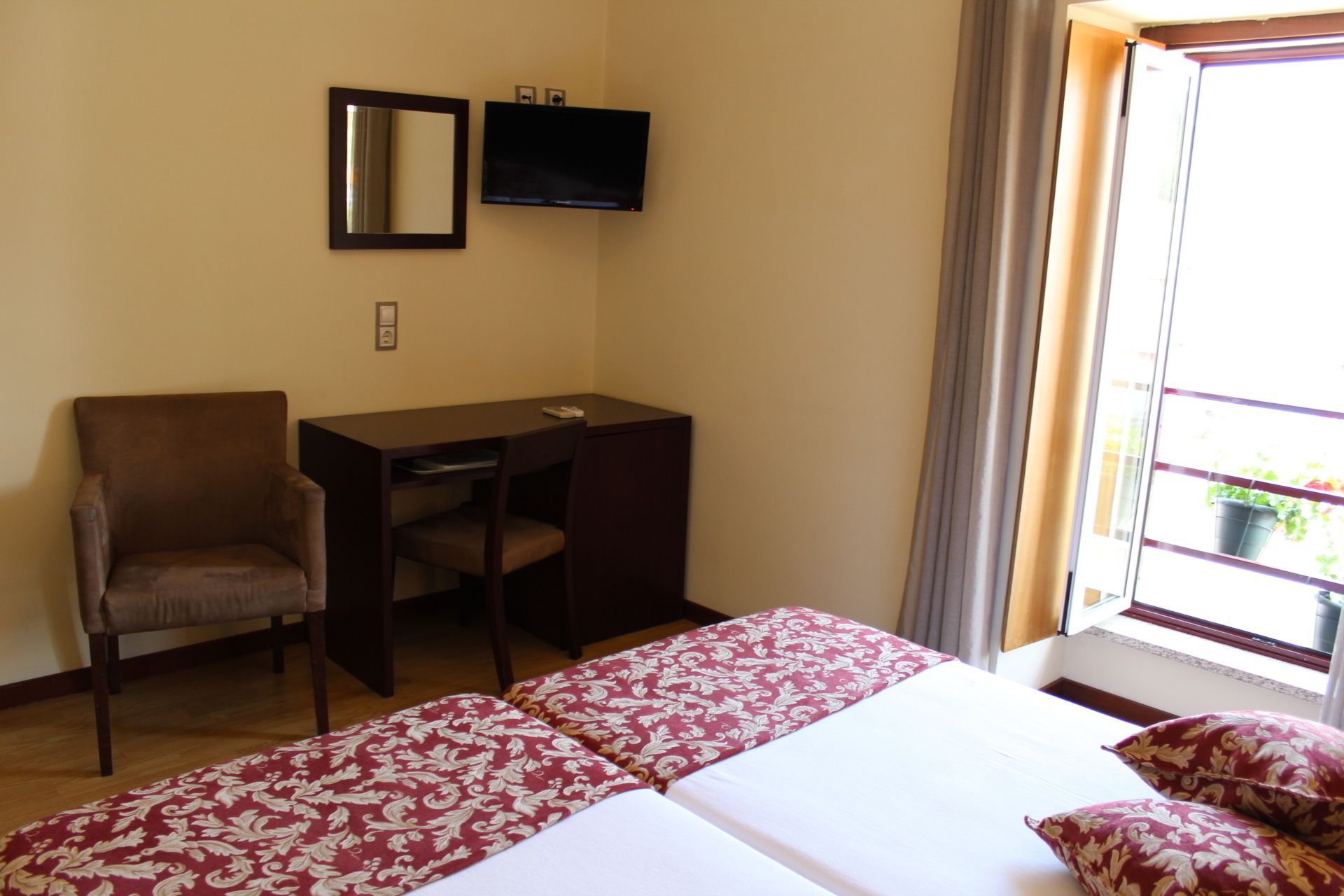 Ein Hotelzimmer mit Bett, Schreibtisch, Stuhl, Fernseher und einem Fenster mit Vorhängen.