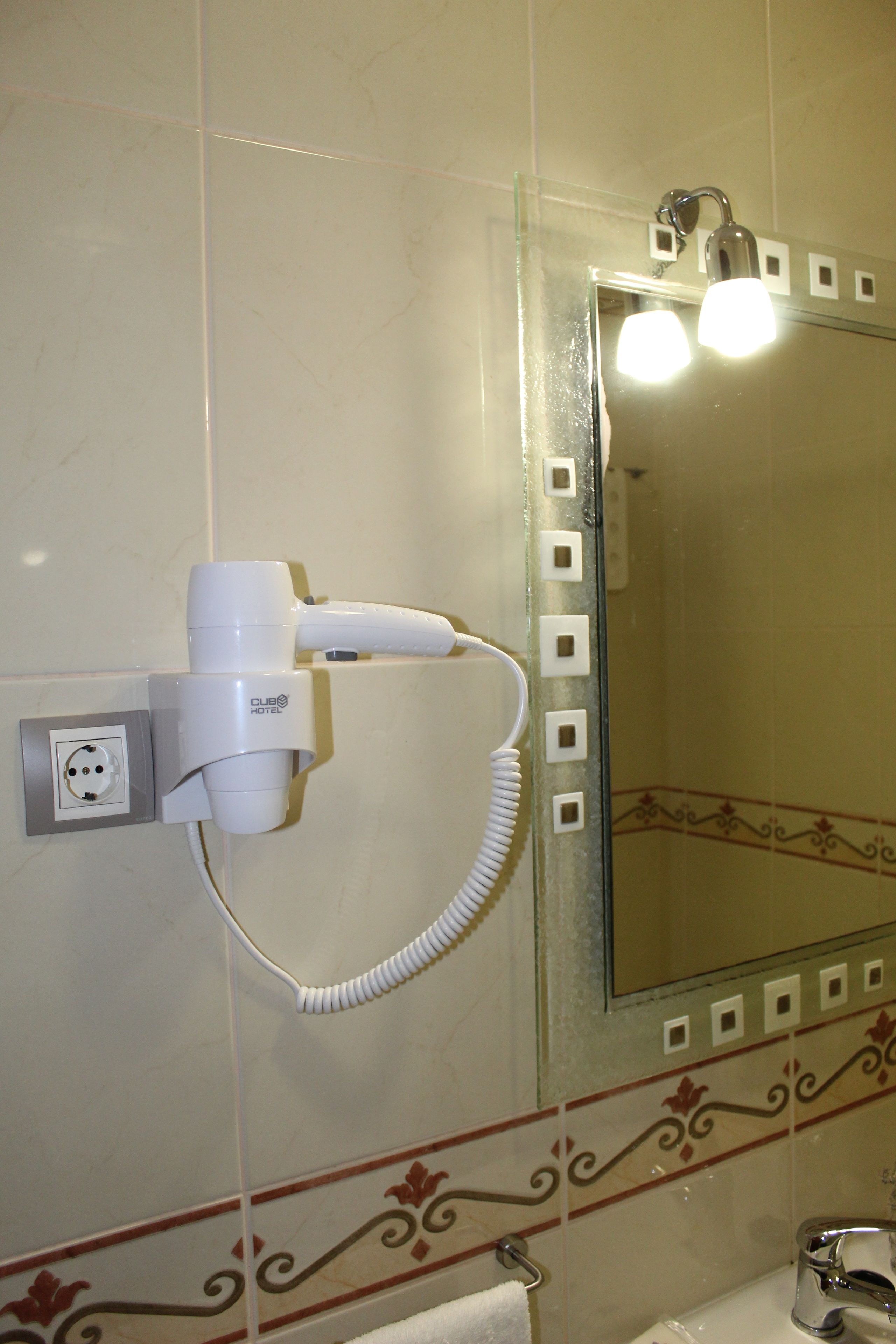 Un baño con un secador de pelo montado en la pared, un perchero y un espejo con azulejos decorativos.