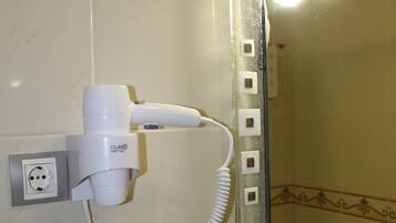 Un baño con un secador de pelo montado en la pared, un perchero y un espejo con azulejos decorativos.