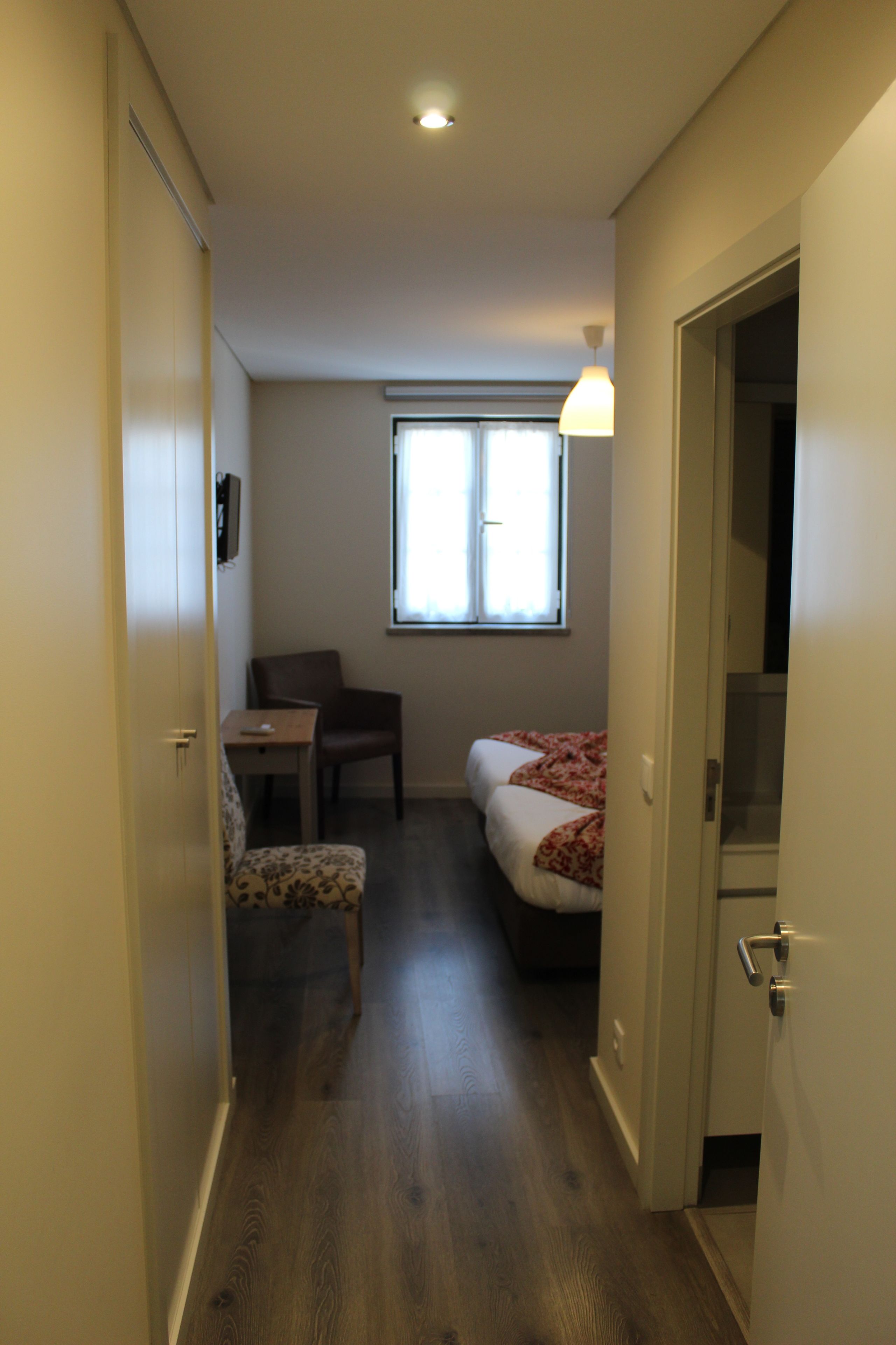 A narrow hallway leading to a bedroom with a single bed, a chair, and a table.