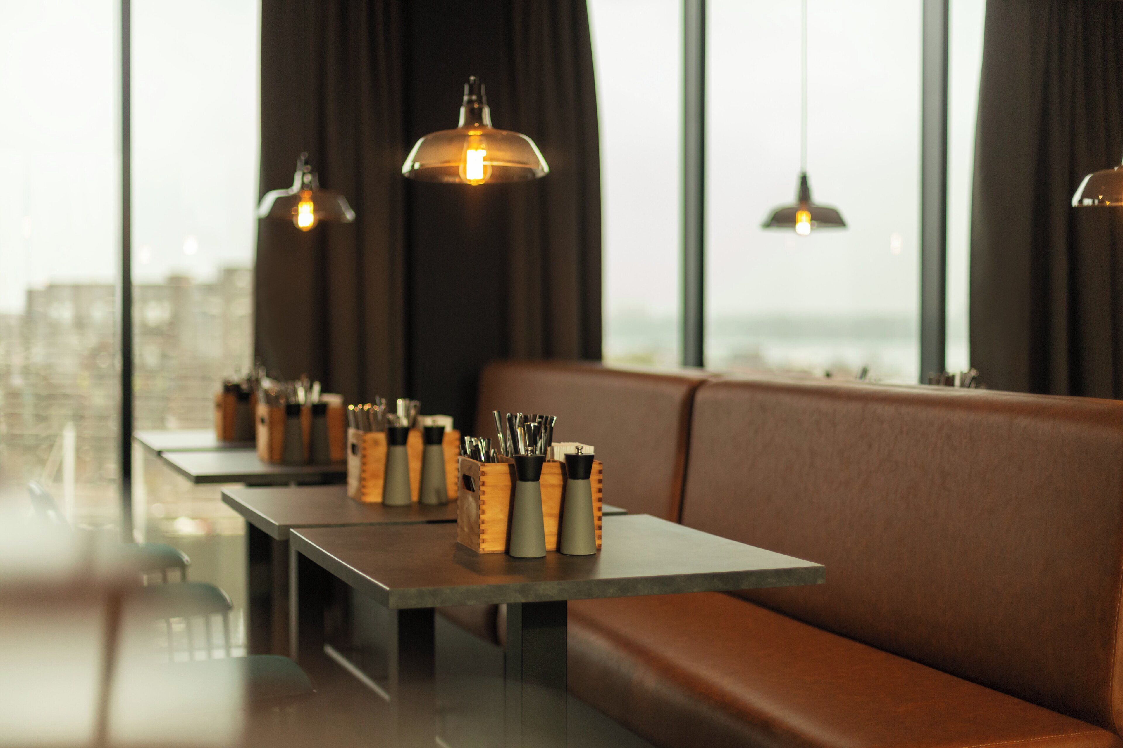 Un restaurante moderno con asientos de cuero, mesas de madera e iluminación colgante.