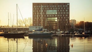 Marina con barcos amarrados, un edificio moderno con amplias ventanas y una superficie acuática tranquila que refleja las estructuras.