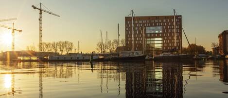 Escena costera con un edificio moderno, barcos y grúas.