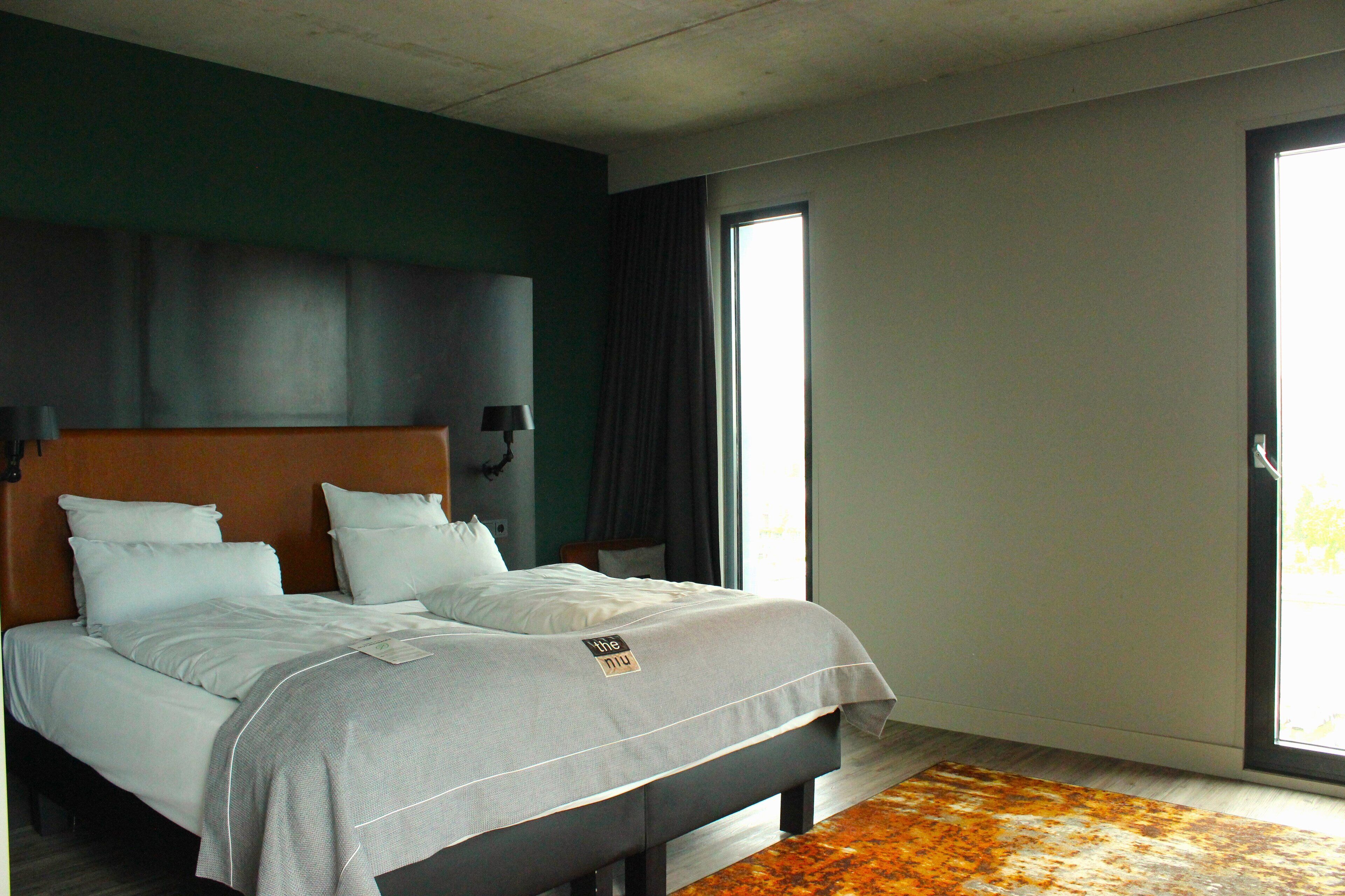 Una habitación de hotel moderna con una cama grande, paredes verde oscuro y vistas al exterior a través de una puerta corrediza.