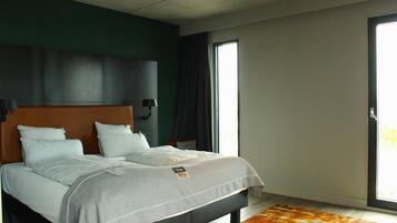 Una habitación de hotel moderna con una cama grande, paredes verde oscuro y vistas al exterior a través de una puerta corrediza.